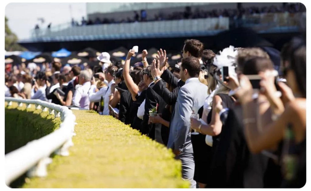 A crowd of people taking pictures at a horse race.